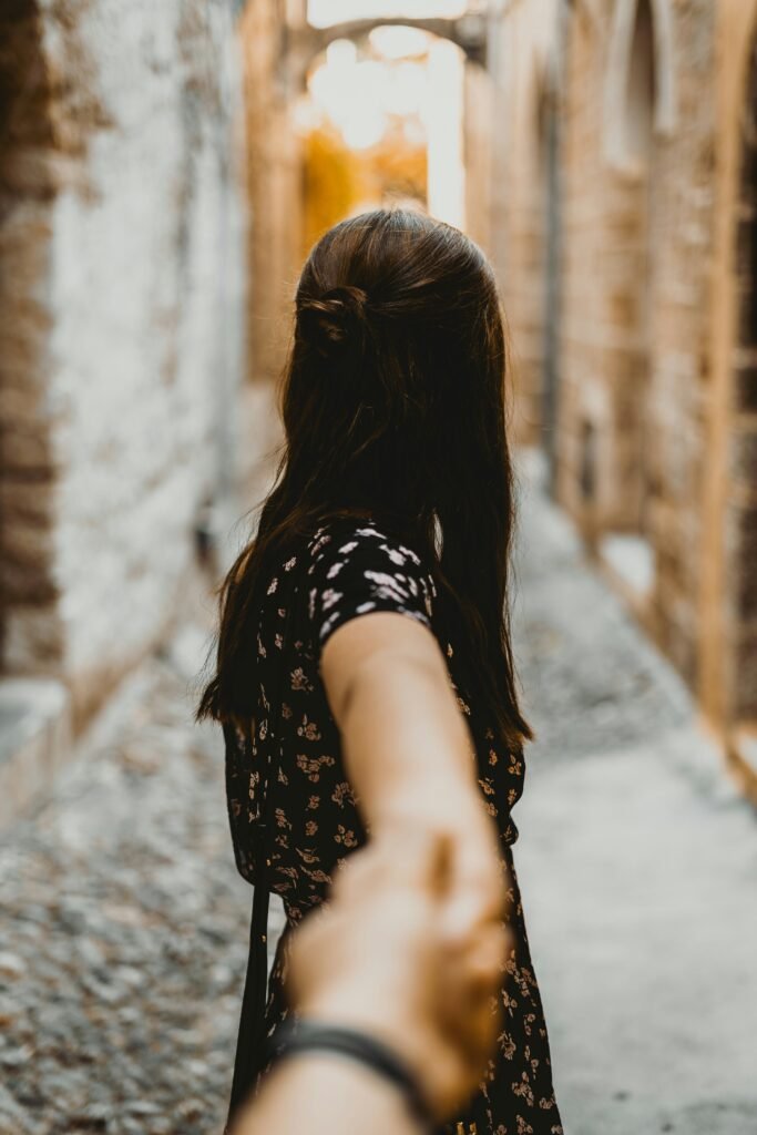 A woman holding hands with a partner in a rustic alleyway, symbolizing love and connection.